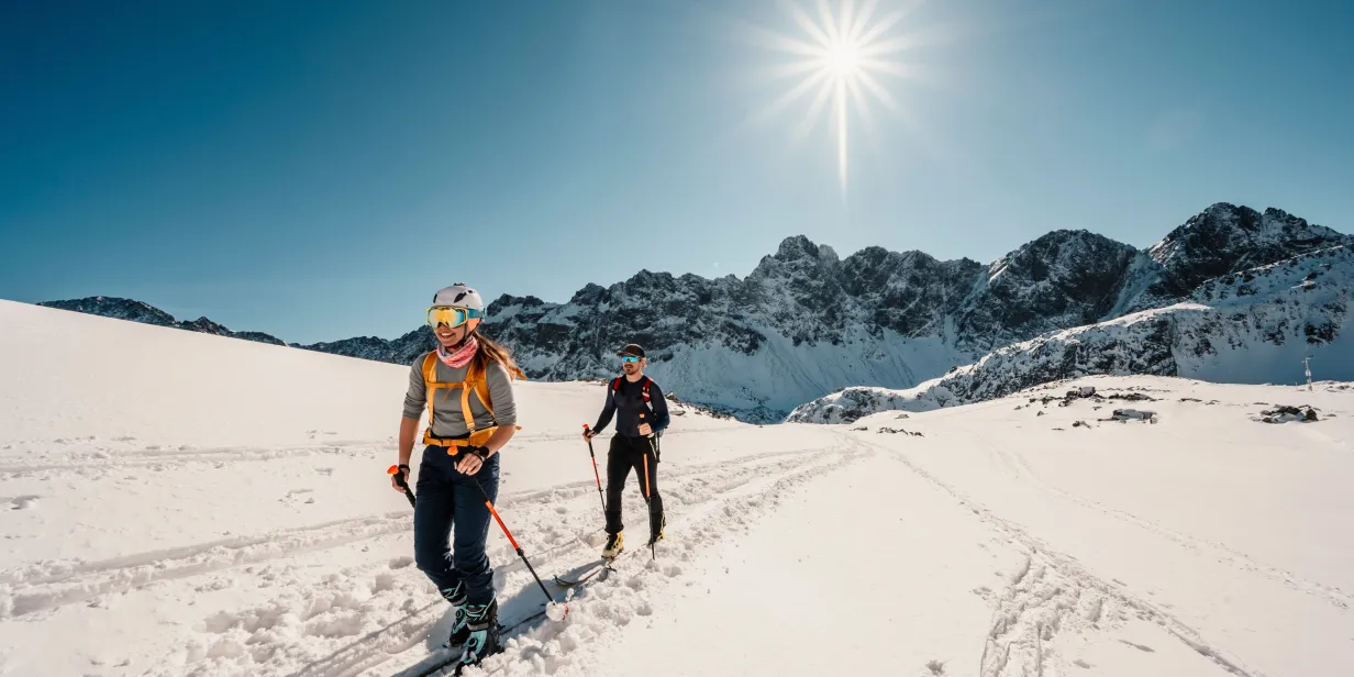 Two skiers descending a snowy mountain slope on a clear day.